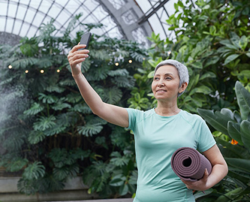 An older adult holding a yoga mat and looking at a smartphone.