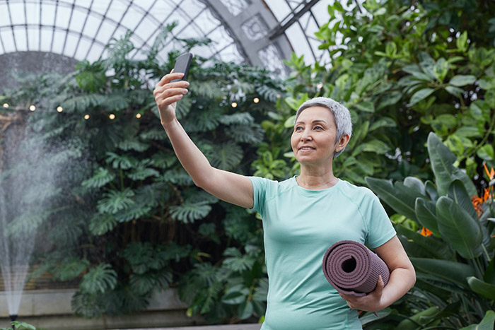 An older adult holding a yoga mat and looking at a smartphone.